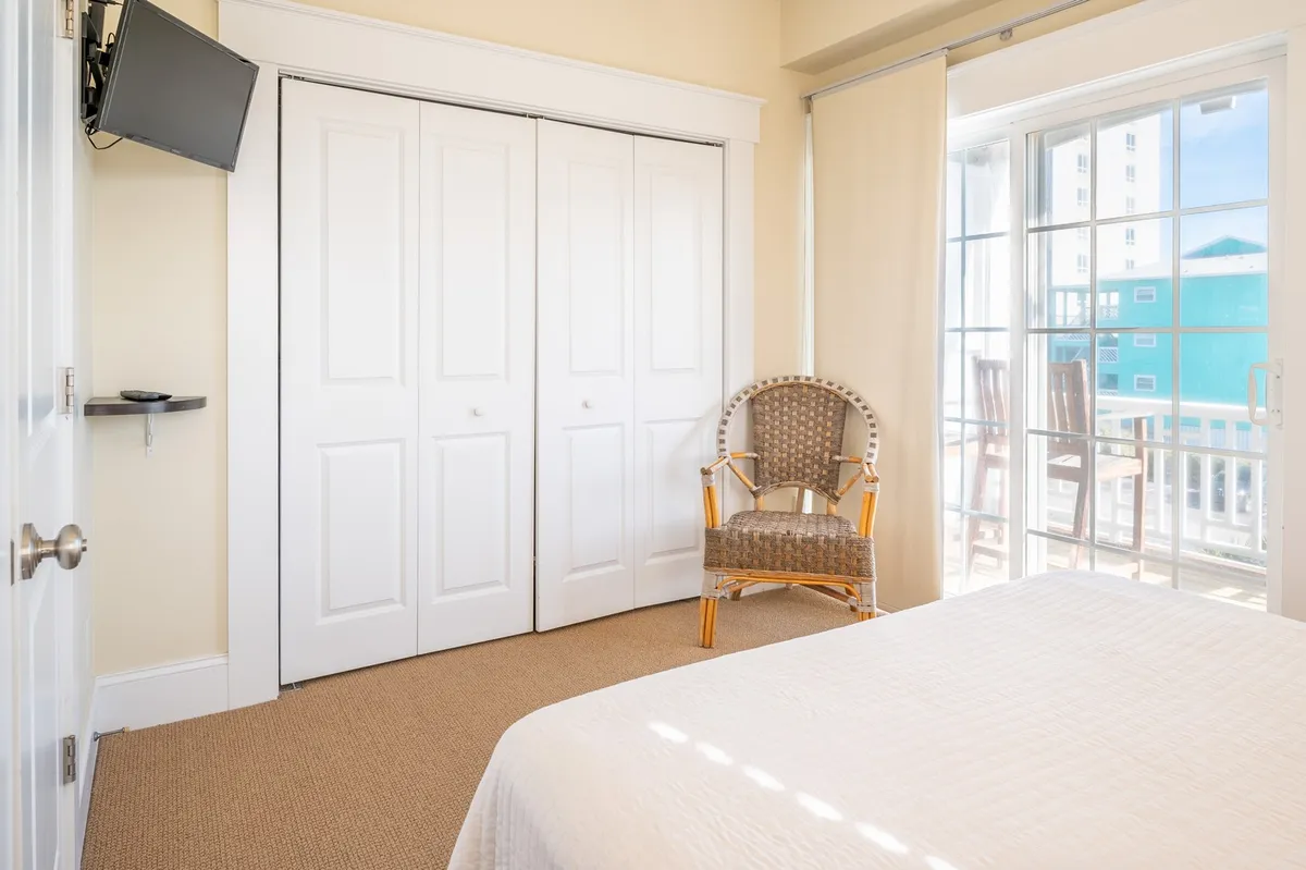 A tranquil bedroom with a comfortable bed, armchair, closet doors, and a sliding glass door leading to a private outdoor space. Natural light streams into the room, creating a warm and inviting place to relax or enjoy the view.