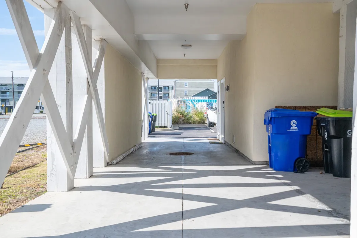 A casual, welcoming entryway space with a visible pathway, entrance, recycling bins, and a bit of landscaping. The area feels connected to the outside, suggesting easy access for guests and pets.