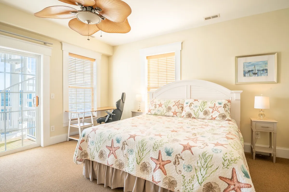 A serene bedroom featuring a bed with a starfish quilt, a desk and chair near a window with blinds, and tranquil natural light filling the room. The space is designed for both relaxation and productivity, with soft textures and a calming color palette.